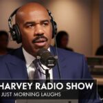 Comedian Steve Harvey smiling and speaking into a studio microphone during a broadcast of his radio show.